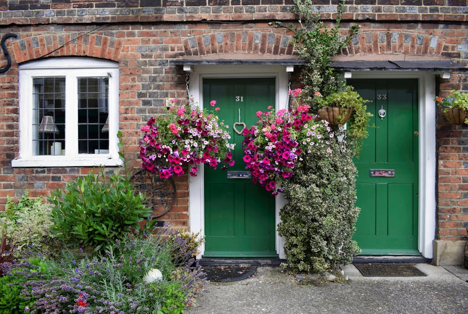 A close-up view of a small front garden in a residential area showcasing two green painted wooden front doors with house numbers 31 and 33, set within a brick façade. The door to number 31 features a